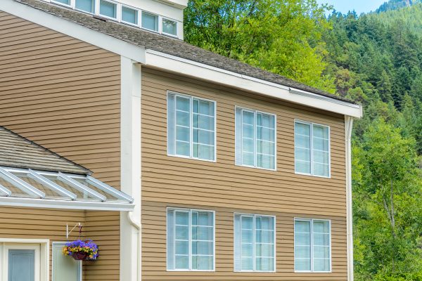 Finished multi-story home with tan vinyl siding beside a forested hillside