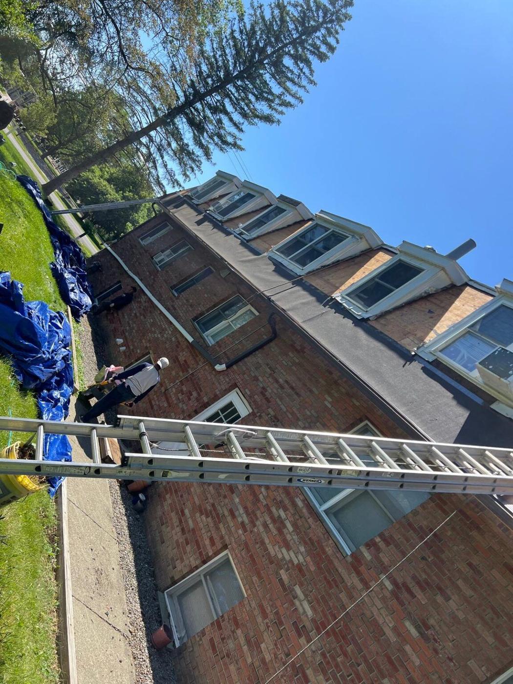 Ladder against a brick multifamily building during a roofing job, tarps staged on the ground