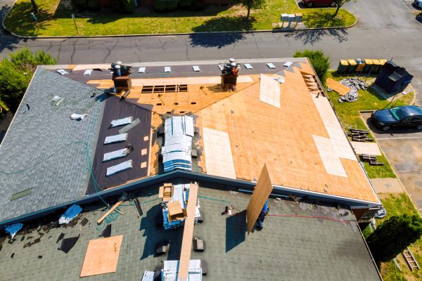 Aerial view of a roof deck mid-installation with plywood sheathing and chimney flashing