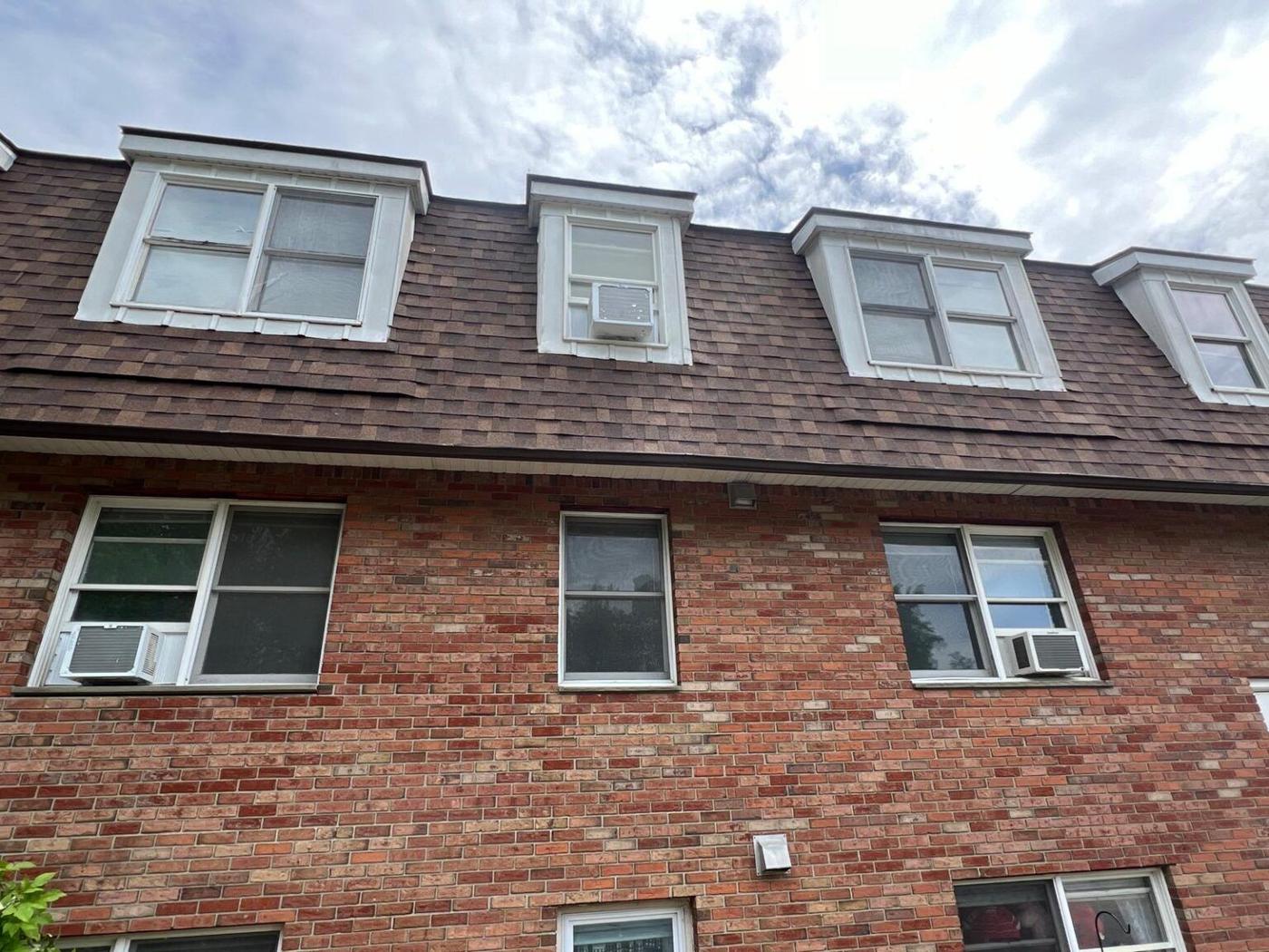 Brick multifamily building with several roof dormers and a new shingle roof